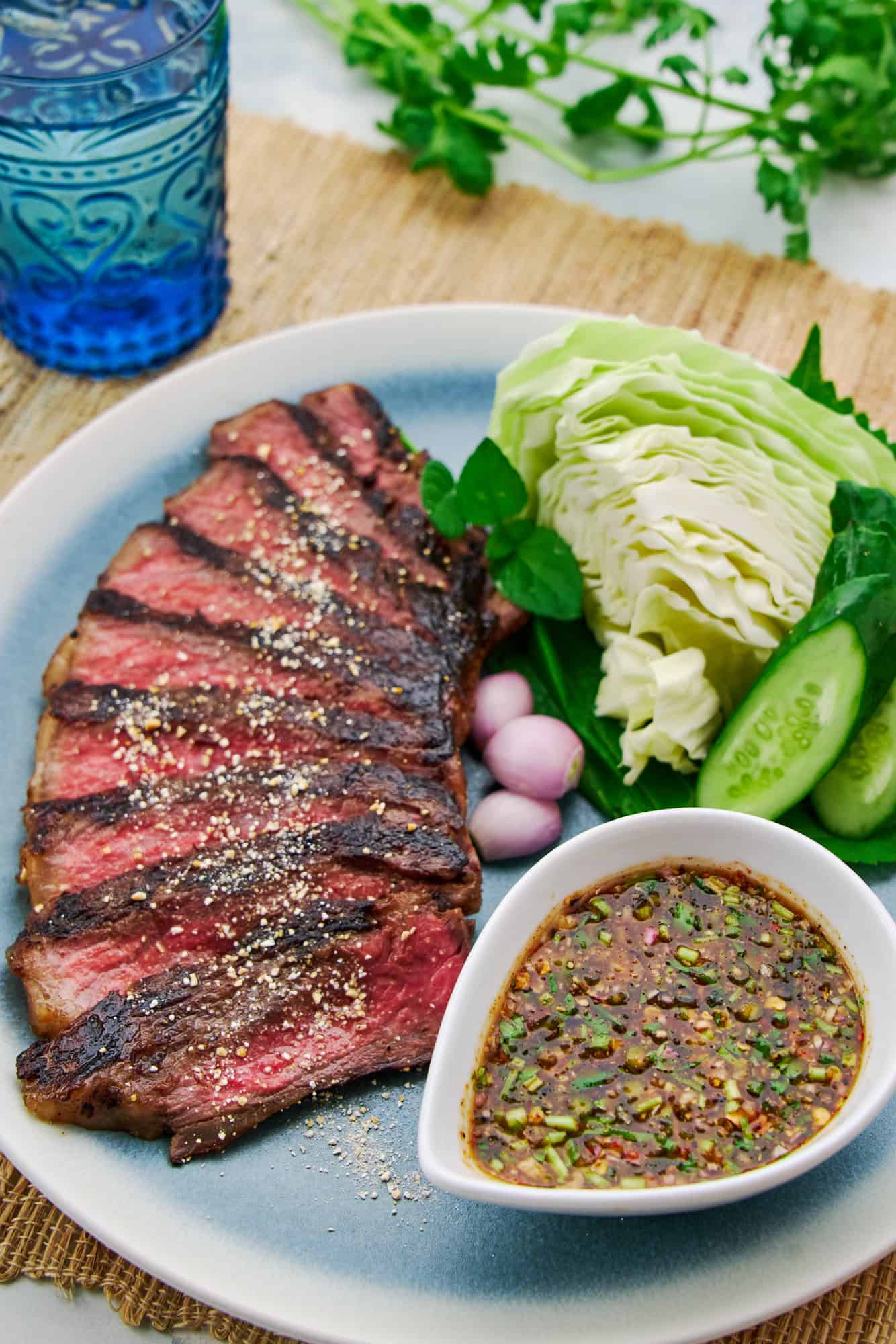 Crying Tiger Beef, highlighting the juicy texture of the meat with crunchy toasted rice and a bowl of vibrant Nam Jim Jaew sauce for dipping the steak.