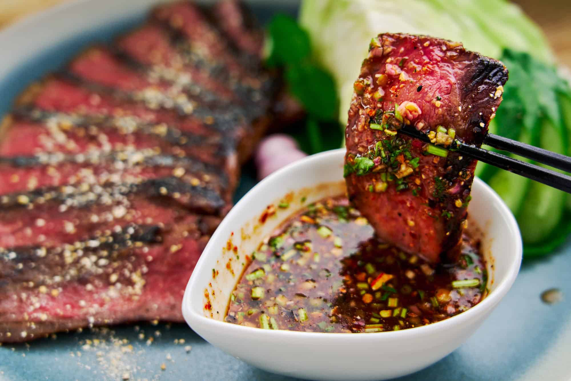 Dipping a medium rare slice of Crying Tiger Beef in spicy Nam Jim Jaew, a spicy tangy and savory Thai BBQ sauce that's addictively good.