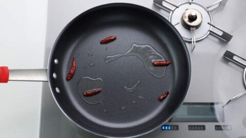 Frying red chili peppers in a large frying pan with oil.
