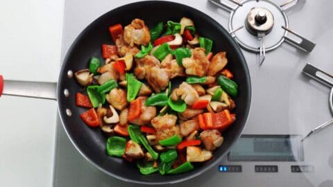 Hunan style chicken with chicken and red and green peppers in a pan.