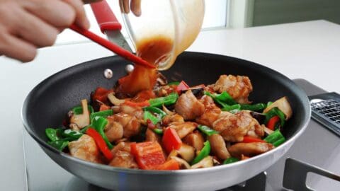 Adding Hunan chicken sauce to a frying pan of chicken and peppers.