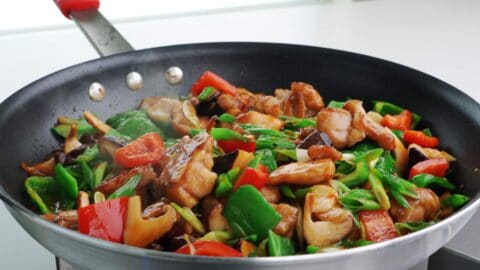 Hunan chicken in a frying pan with marinated chicken, mushrooms, peppers, and scallions.