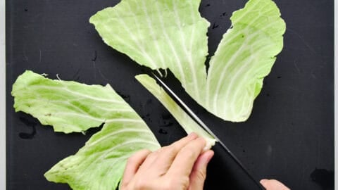 Cutting out the tough central stem from cabbage leaves with a knife.