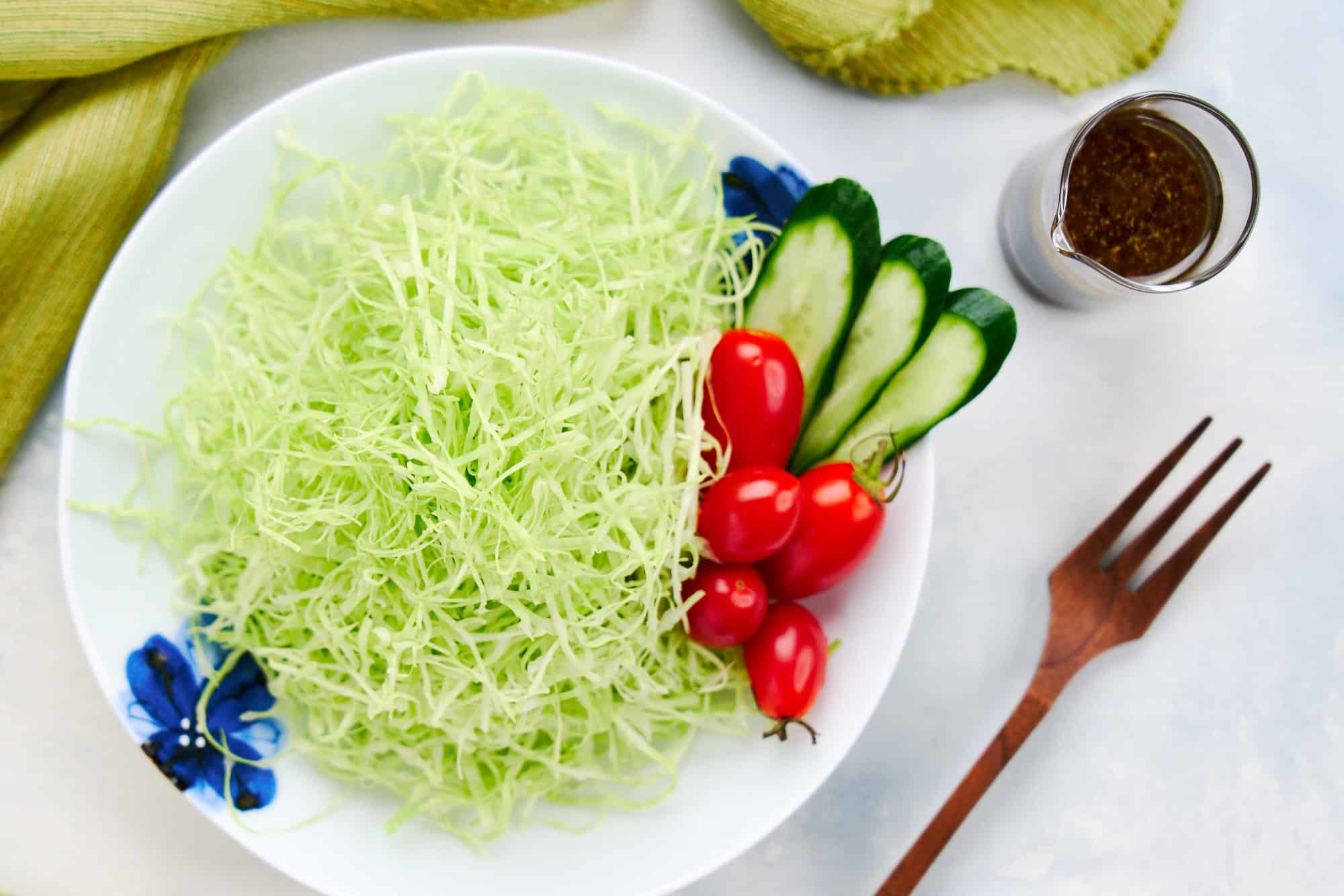 Overhead view of thinly shredded Japanese cabbage salad with cherry tomatoes, cucumber, and dressing.