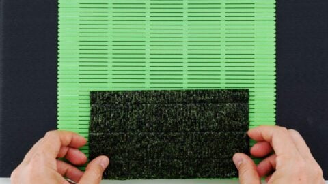 Half sheet of nori placed on the bottom edge of a sushi mat.