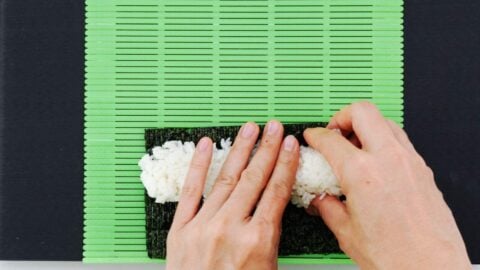 Pressing sushi rice across a sheet of nori.