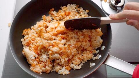 Stir-frying kimchi rice in a frying pan with a spatula.