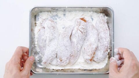 Dusting chicken fingers with flour.