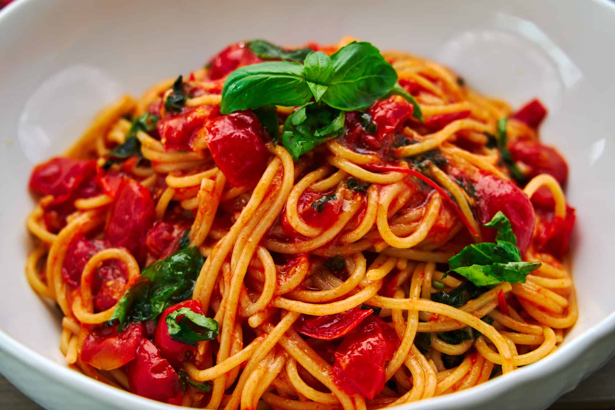 Side-view of a bowl of Pasta Pomodoro, showing the depth and layers of spaghetti intertwined with chunks of ripe tomatoes and basil leaves.