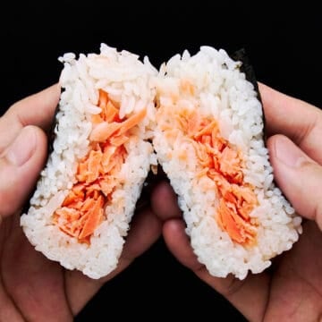Salmon Onigiri split in half showing tender salted salmon flakes wrapped in a fluffy layer of Japanese short grain rice.