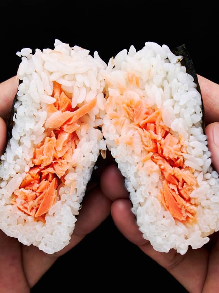 Salmon Onigiri split in half showing tender salted salmon flakes wrapped in a fluffy layer of Japanese short grain rice.