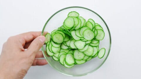 Salting sliced cucumbers in a glass bowl.
